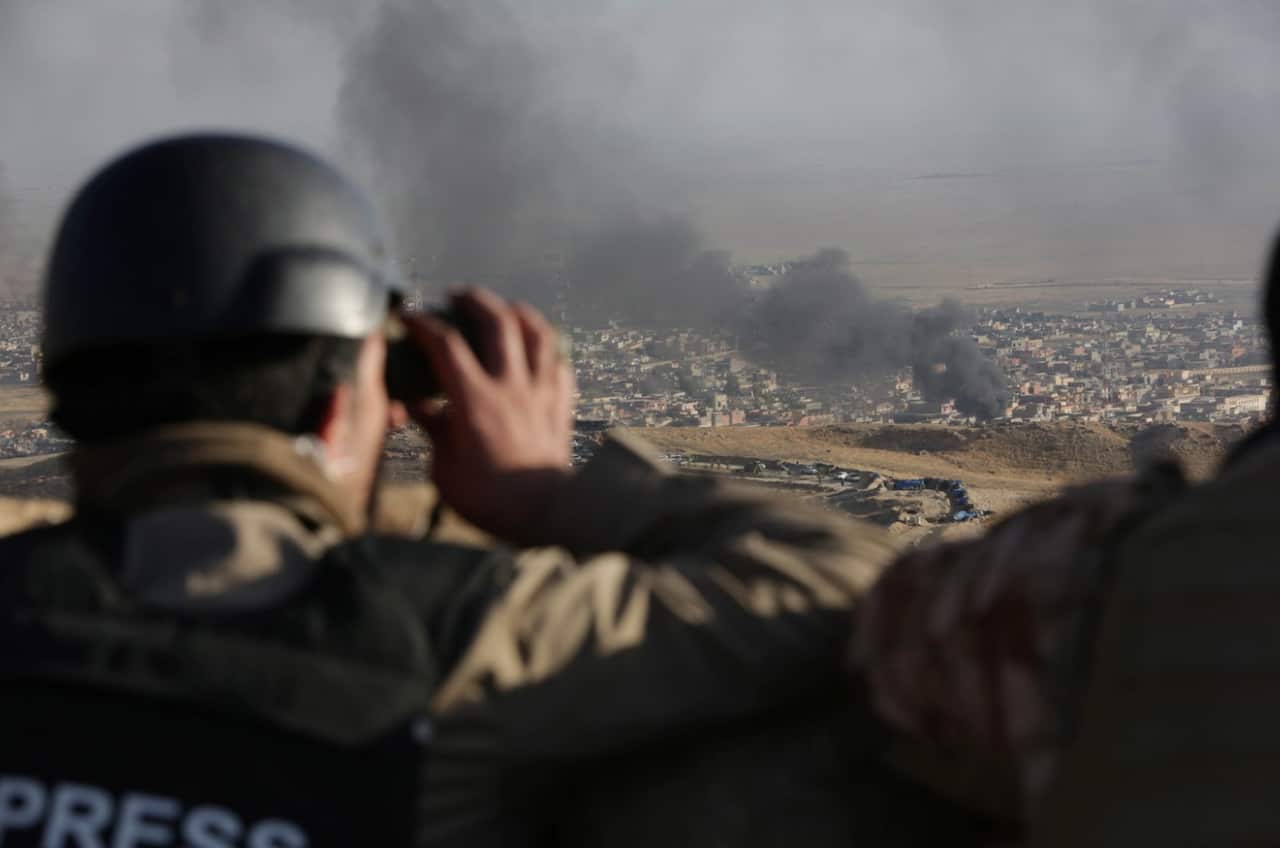 A journalist watches as smoke rises over Sinjar, northern Iraq from oil fires set by IS militants in 2015