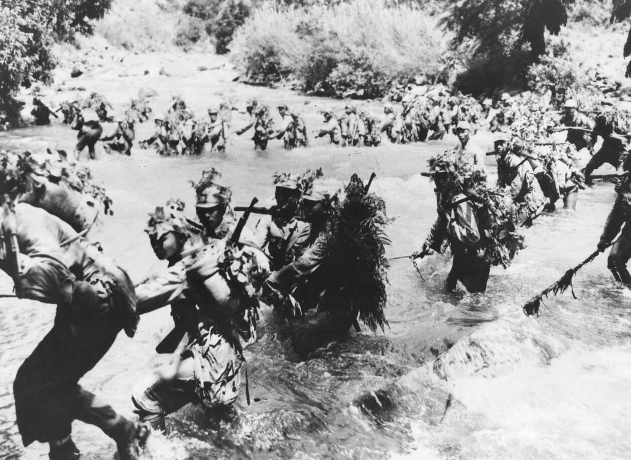 Wearing camouflaged uniforms, Chinese infantrymen ford a stream in southern Yunnan province during the Second Sino-Japanese War.