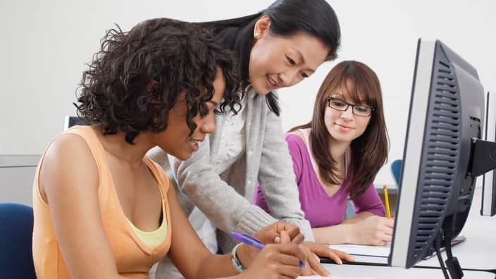 Two female students working with teacher in computer classroom