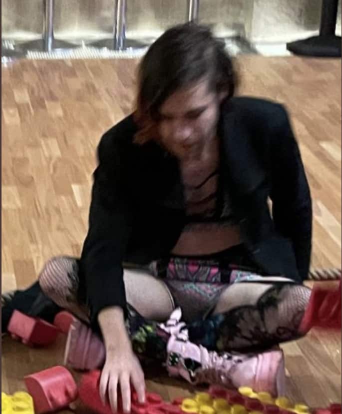 Man in women’s underwear while children play with Lego