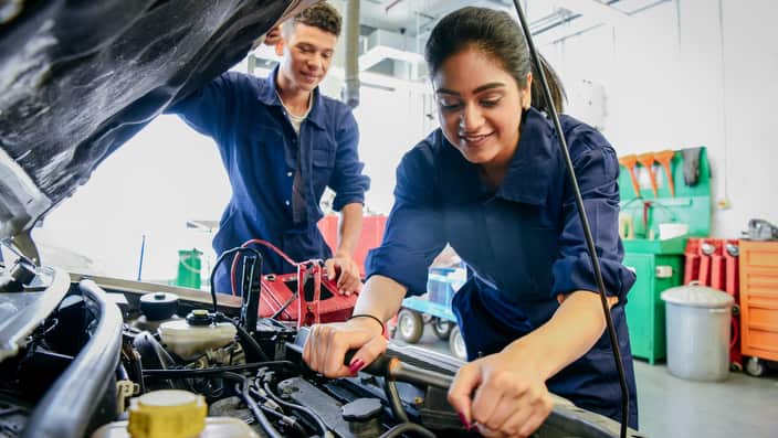 Female mechanic fixing car, young man watching