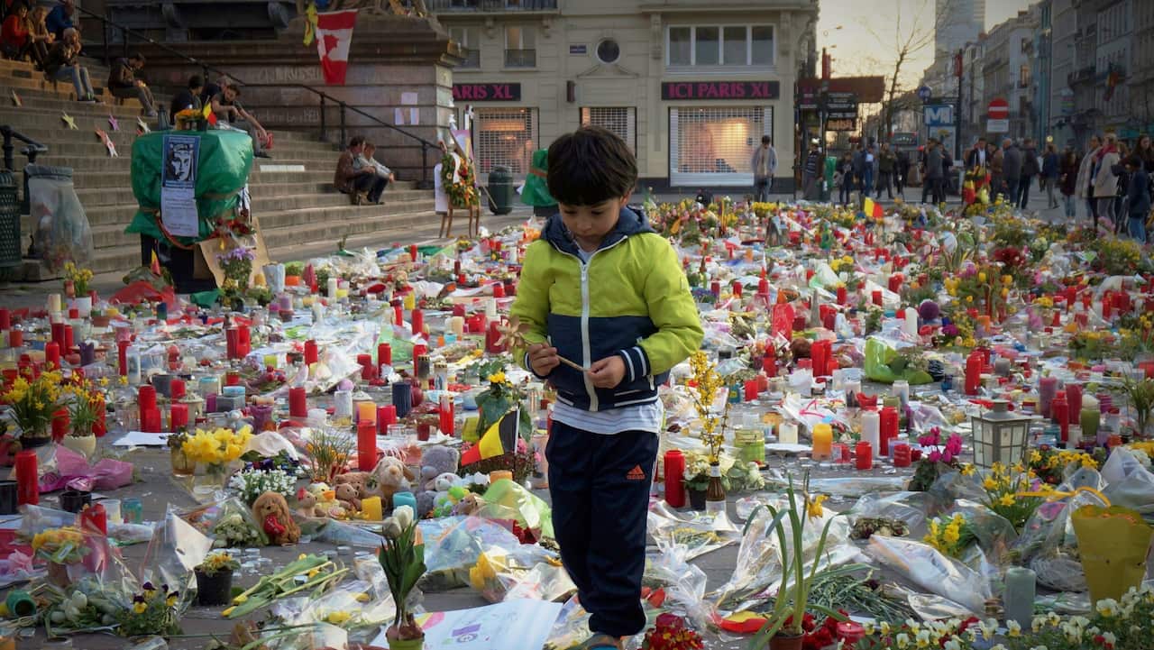 Boy in a field of flowers and candles laid there for the commemoration of the Brussels terror attacks of 22 March 2016