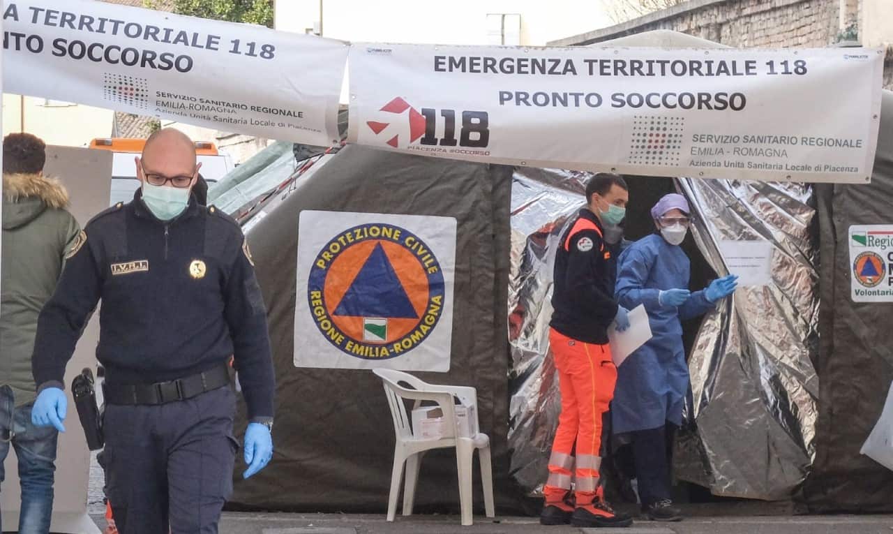 Healthcare professionals wearing protective suits and masks in front of the advanced medical unit built up outside the emergency room of the hospital