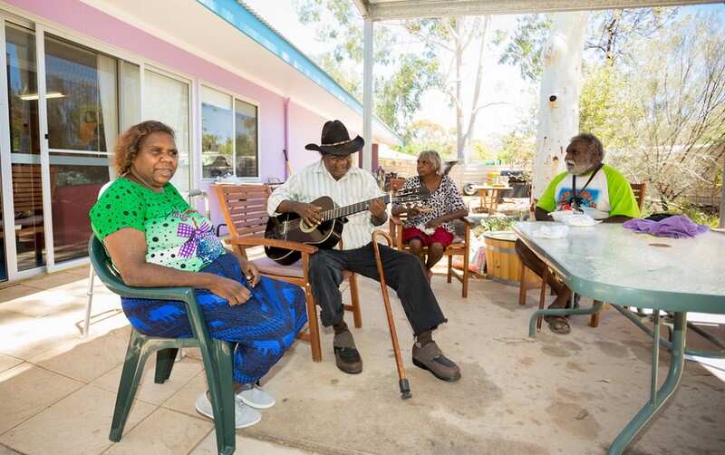Daniel Brumby playing the guitar, with Lorraine outside the Purple House