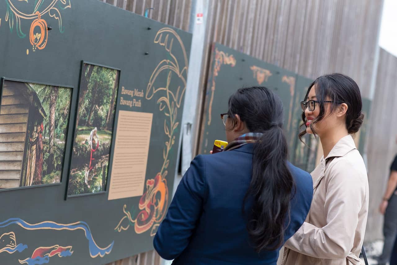 Two visitors examining the legend of Red Onion and White Onion (Bawang Merah, Bawang Putih) characters.