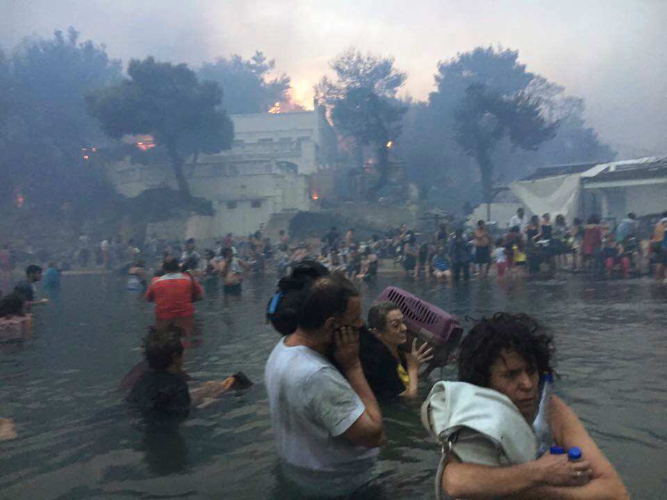 In this Monday, July 23, 2018 image from video, people escaping wildfires wade into the waters of the "Silver Coast" beach in Mati.