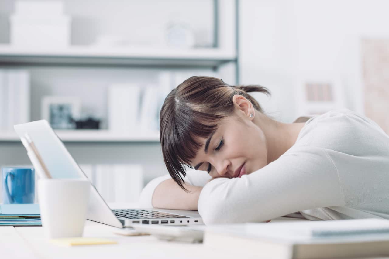 Young tired woman at office desk sleeping with eyes closed, sleep deprivation and stressful life concept
