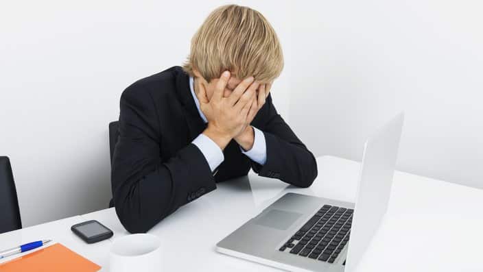 Tired businessman with hands on face sitting at desk by laptop
