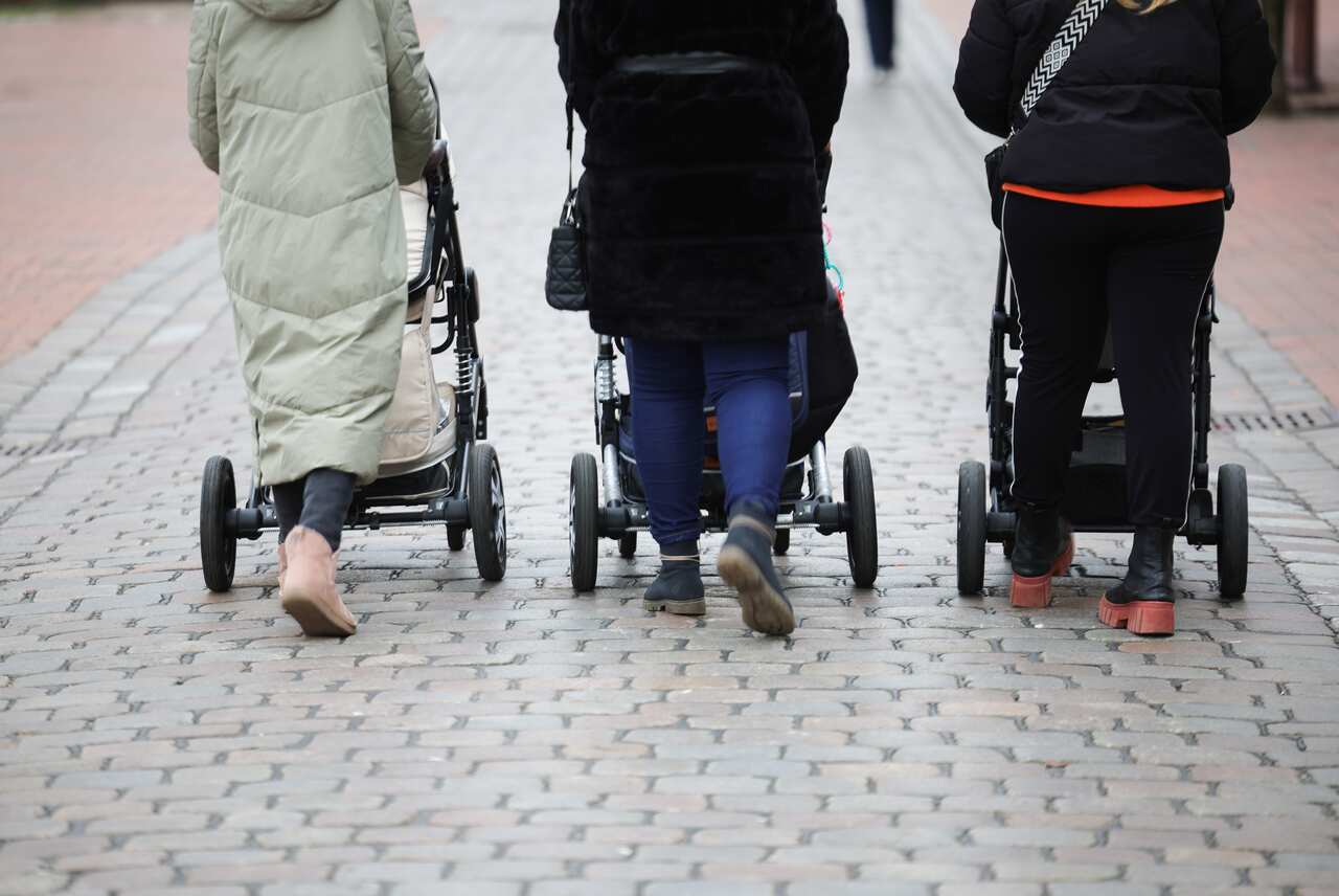 Three women, wearing warm clothes, are walking while pushing baby prams.