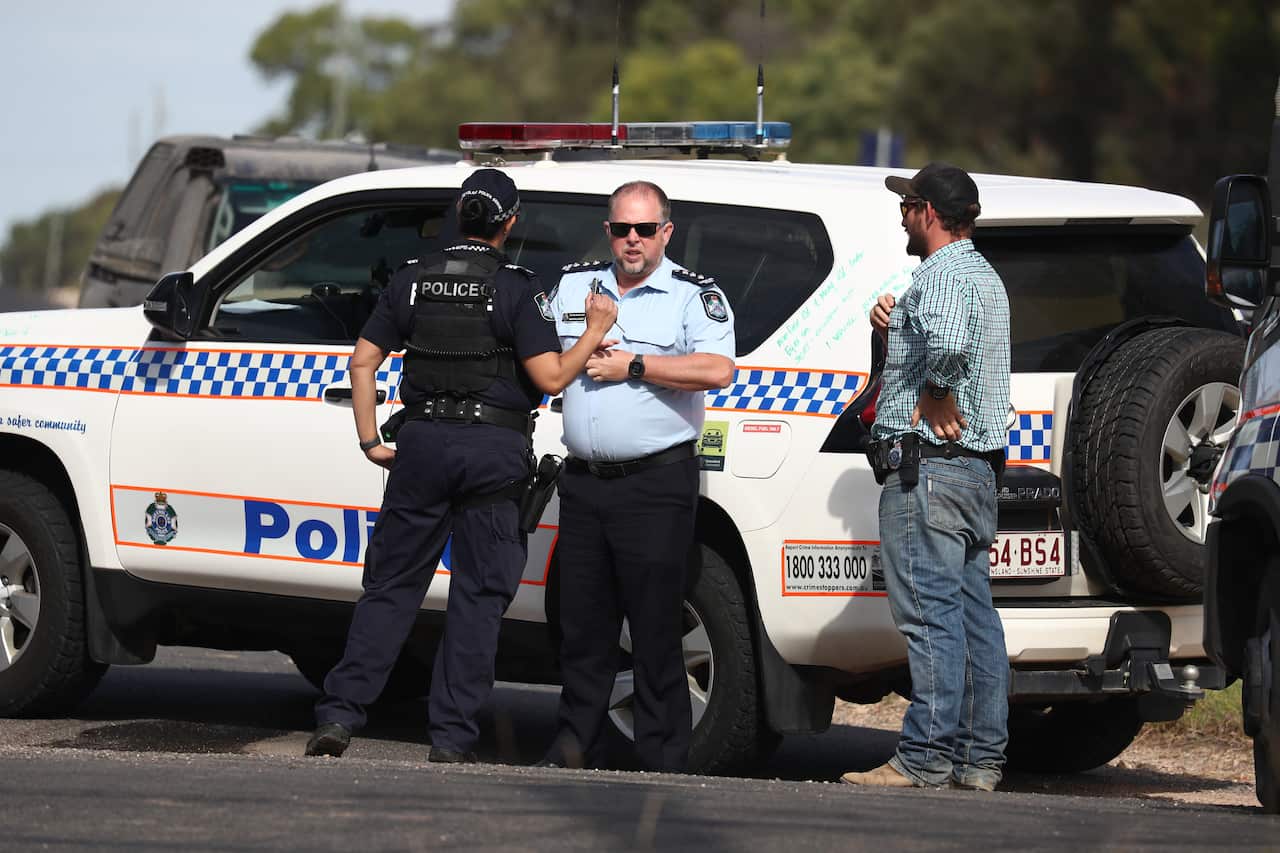 Police officers standing on the road in front of a vehicle that is parked.