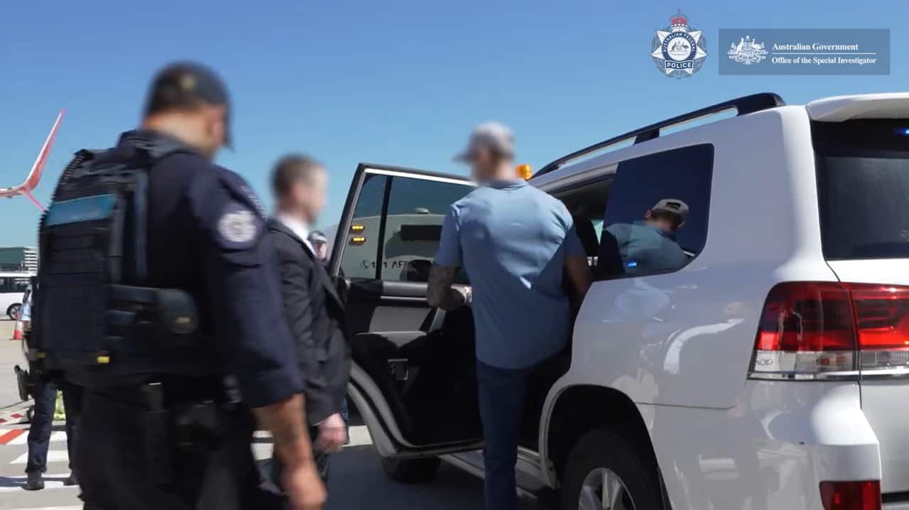 Police escorting a man to a vehicle.