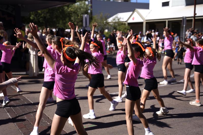 Dozens of young girls in pink t-shirts dance in the sun
