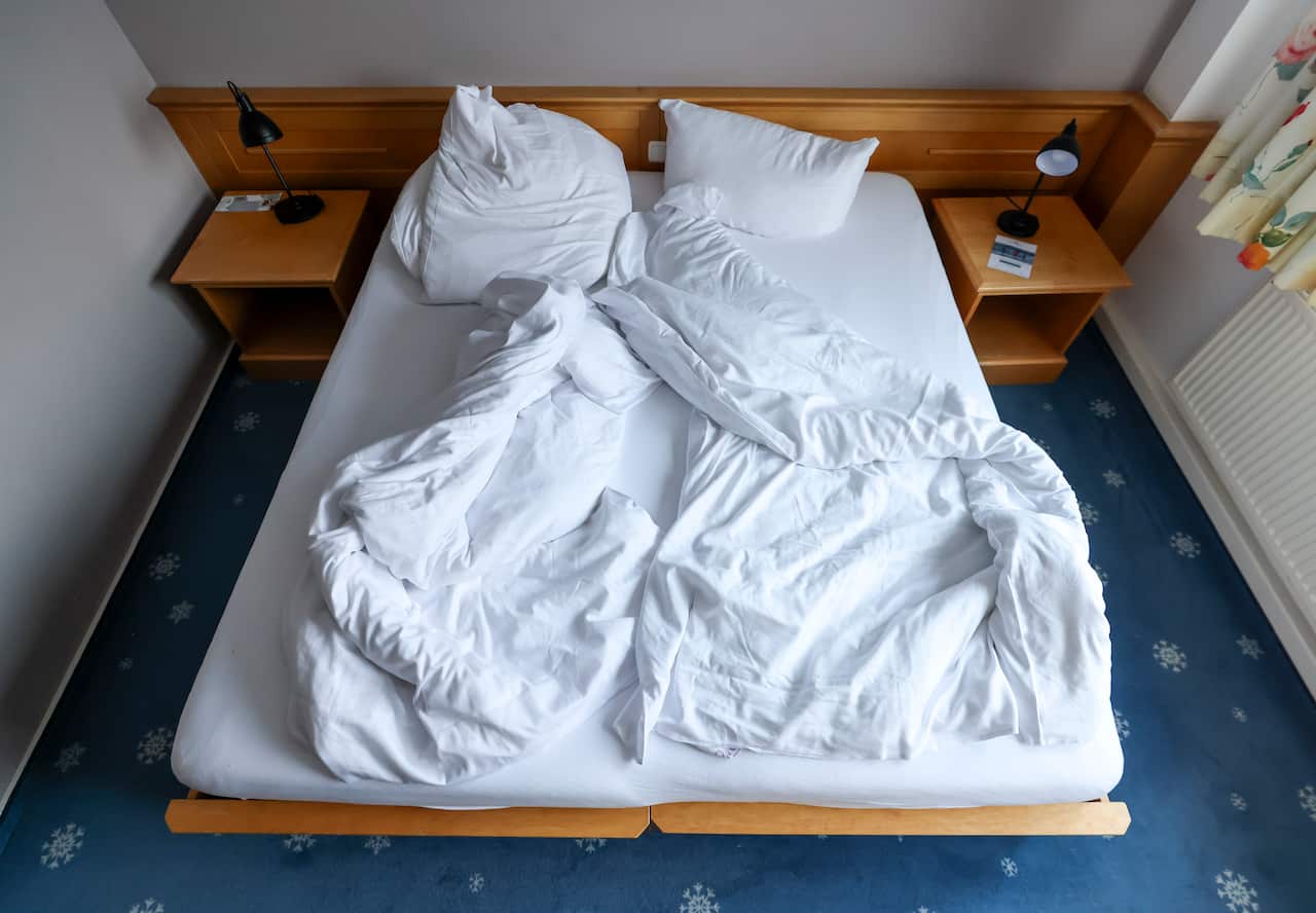 An unmade bed with a white sheet, matching quilts, and pillows.