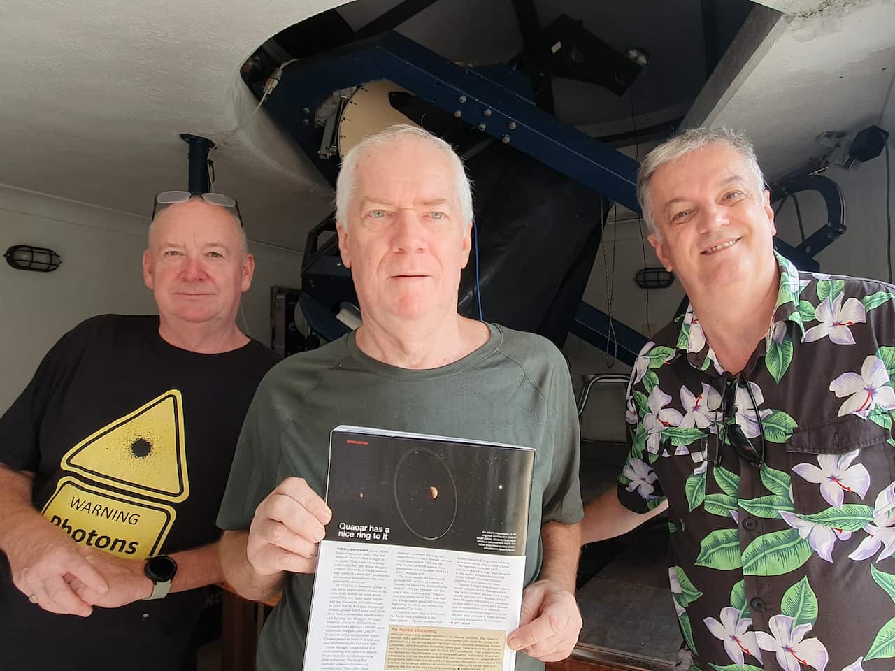 Jonathan, John and Renato stand next to each other and look at the camera as John holds up their published article