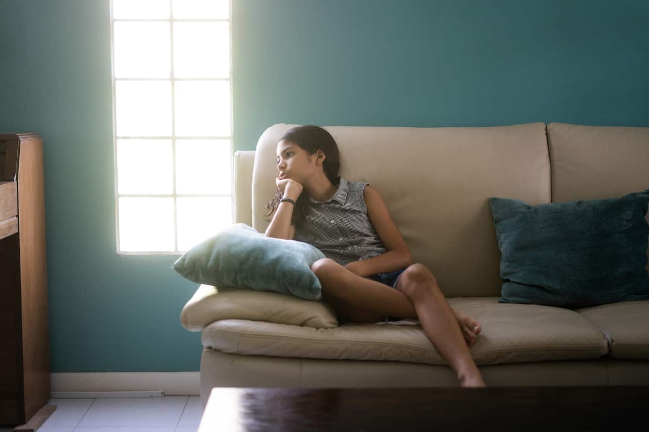 A young girl sitting on a couch looking to the side.