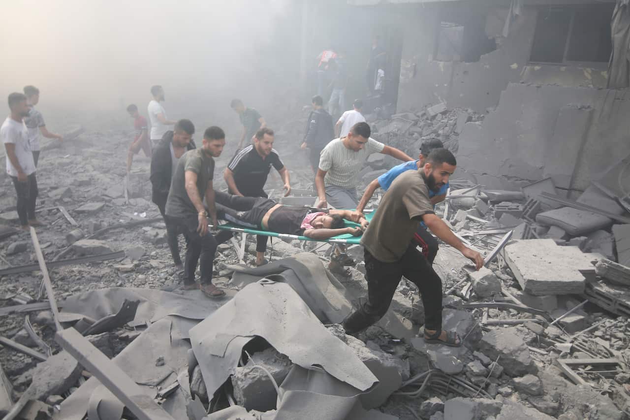 A wounded person is carried on a stretcher through rubble