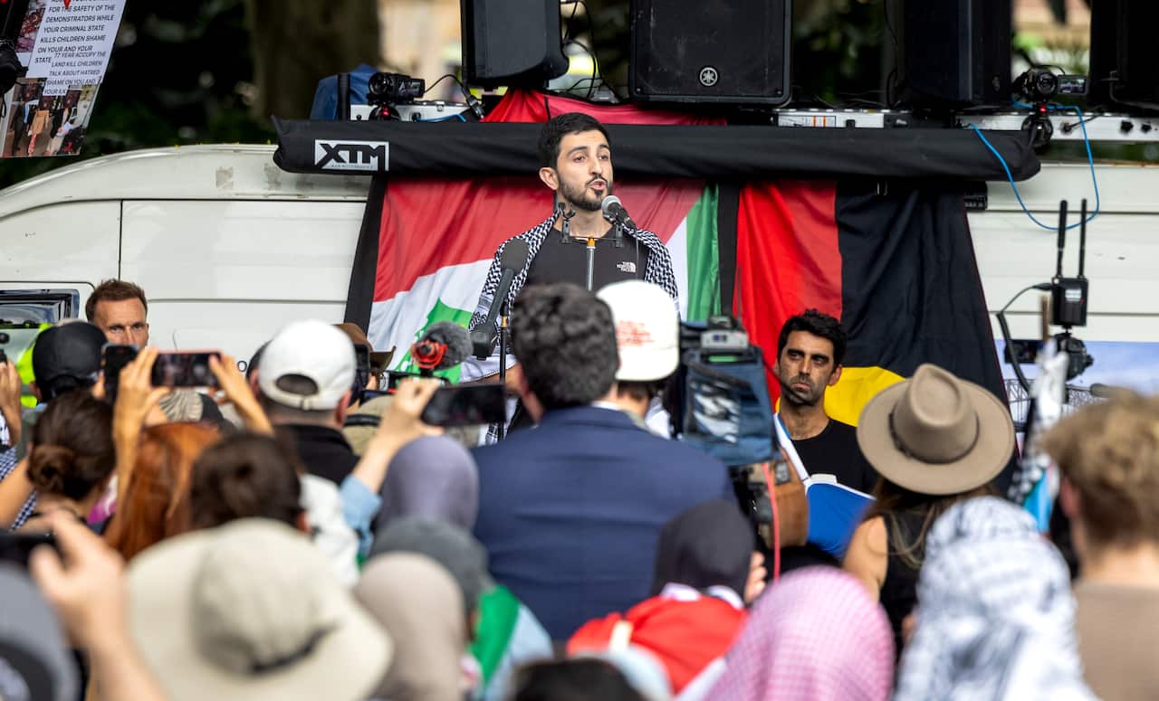A person speaking on stage with a crowd in front of them.