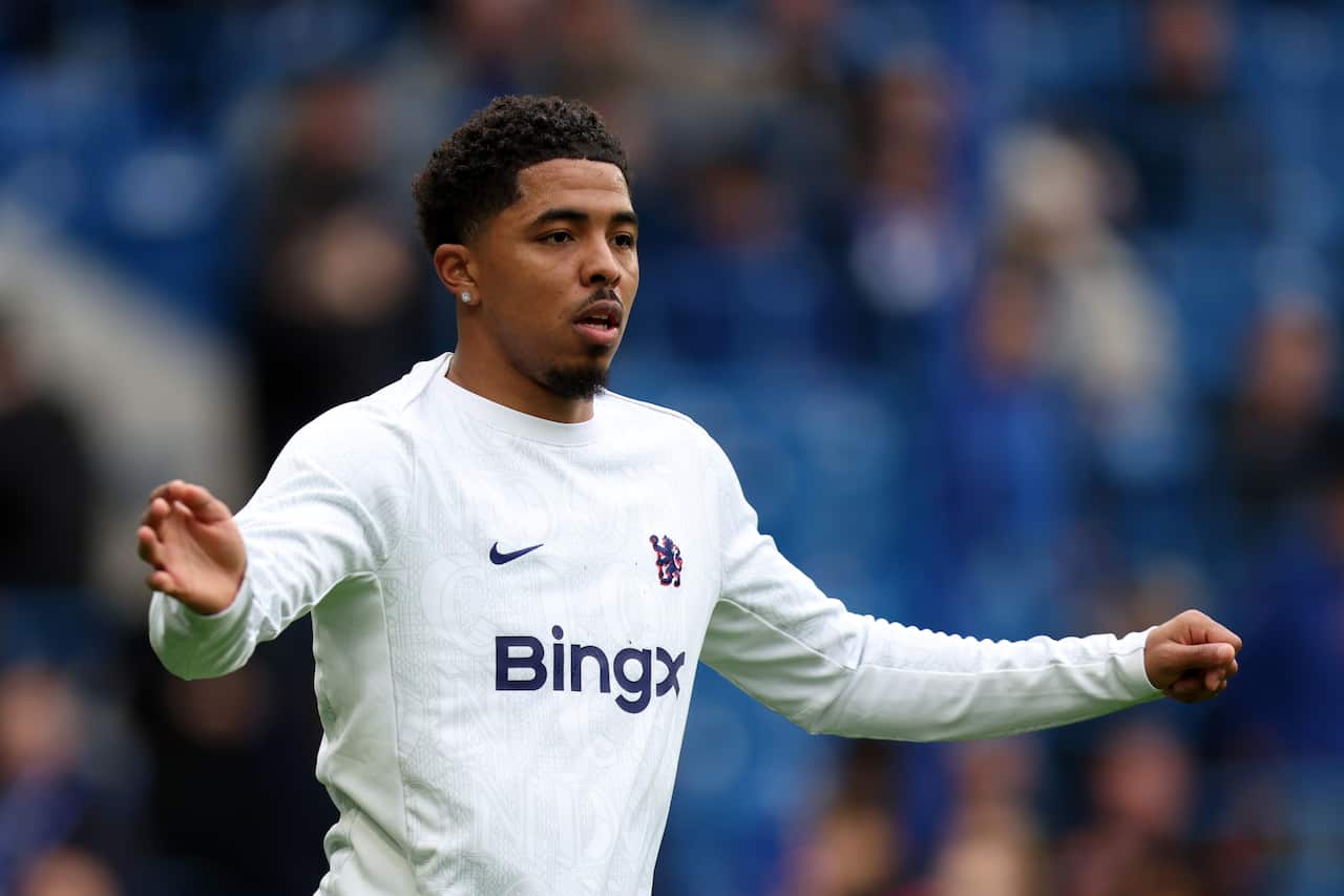 A black athlete wearing a white long-sleeve jersey in front of a blurred background that appears to be of a crowd watching on.