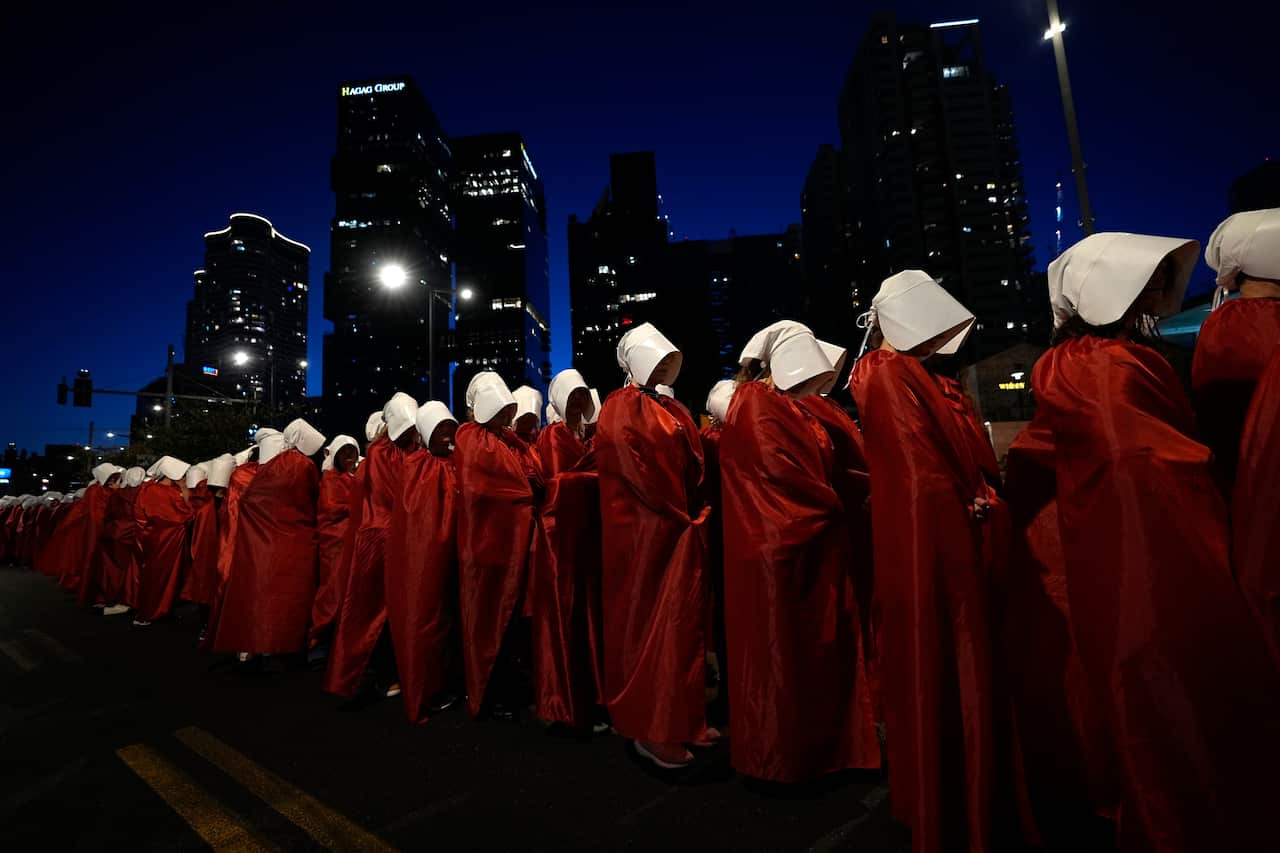 People wearing red dresses and white bonnets stand in a line to protest.