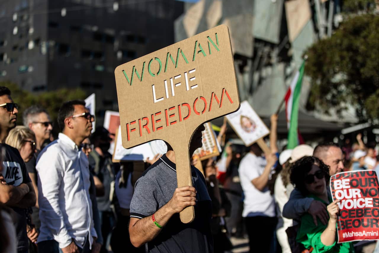 A person holds a sign reading 'WOMAN, LIFE, FREEDOM' during a rally