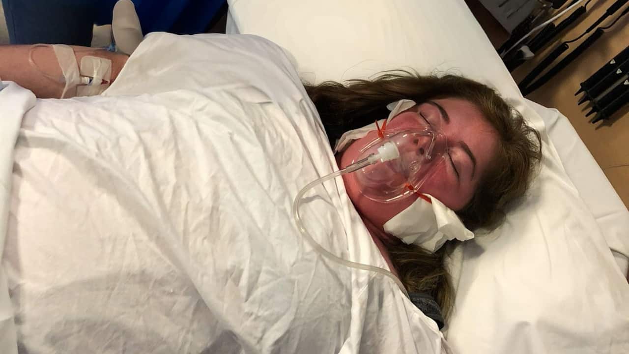 a young woman in a hospital bed with an oxygen mask over her mouth and an IV drip going into her arm