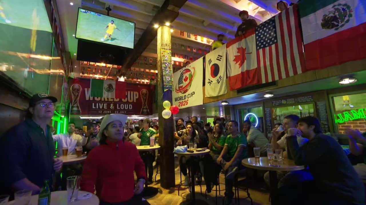 People gathered in a bar to watch a football game, the flags of various countries hang over a balcony