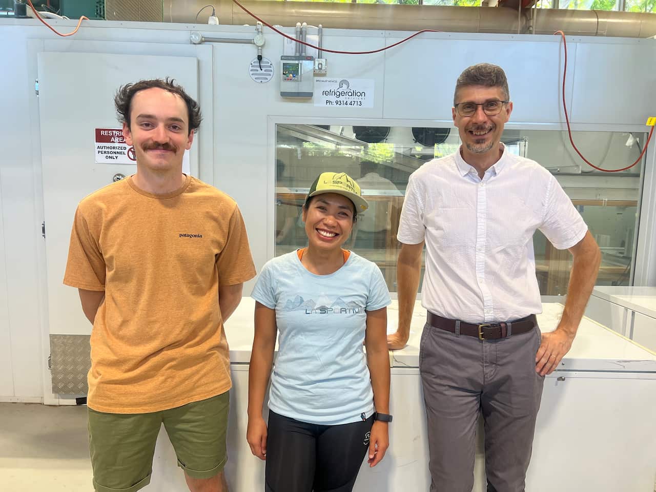 Three people stand in front of a fridge, smiling.