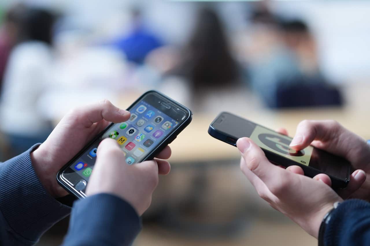 Two school children scrolling on their phones.