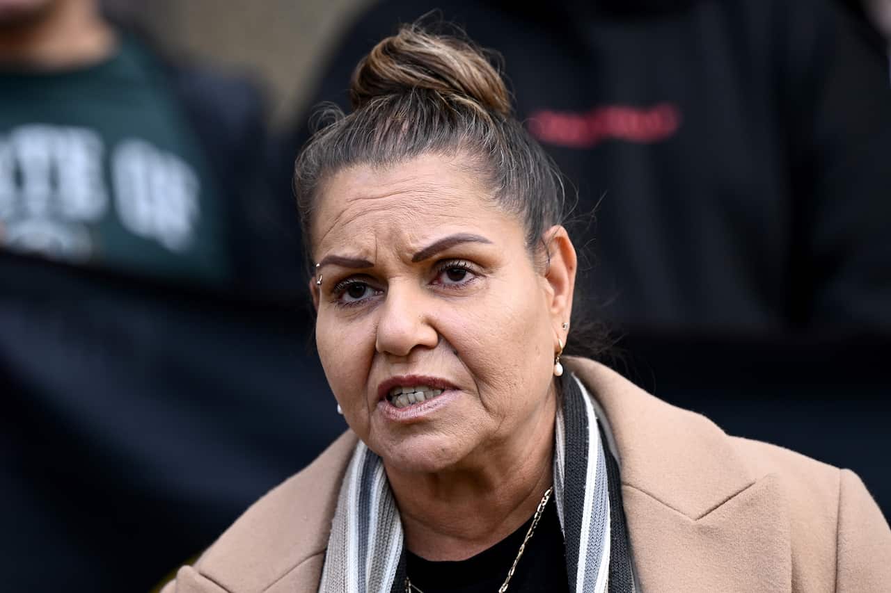 A woman wearing a light brown coat speaking.