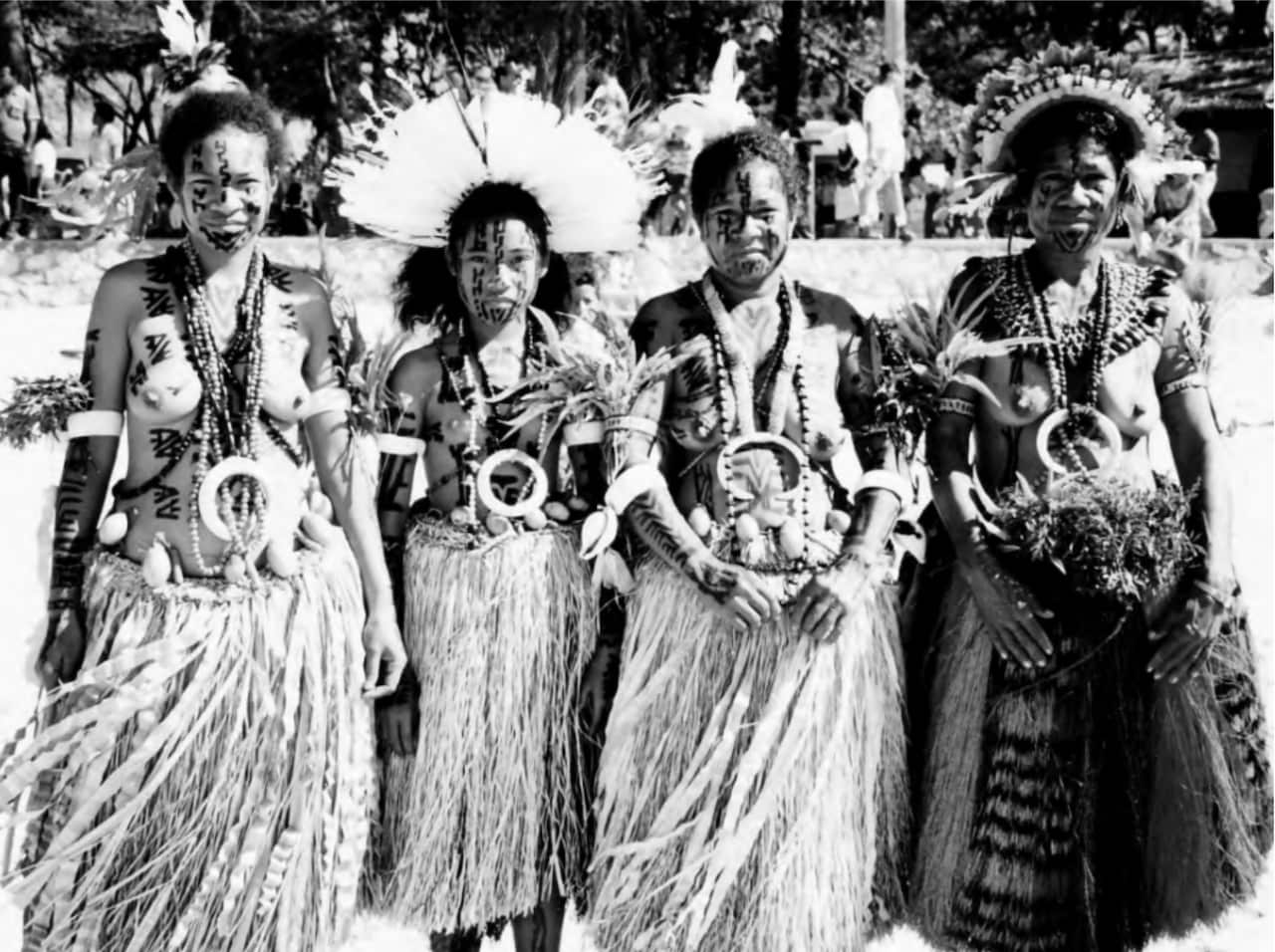 A black and white photo of four topless women in grass skirts