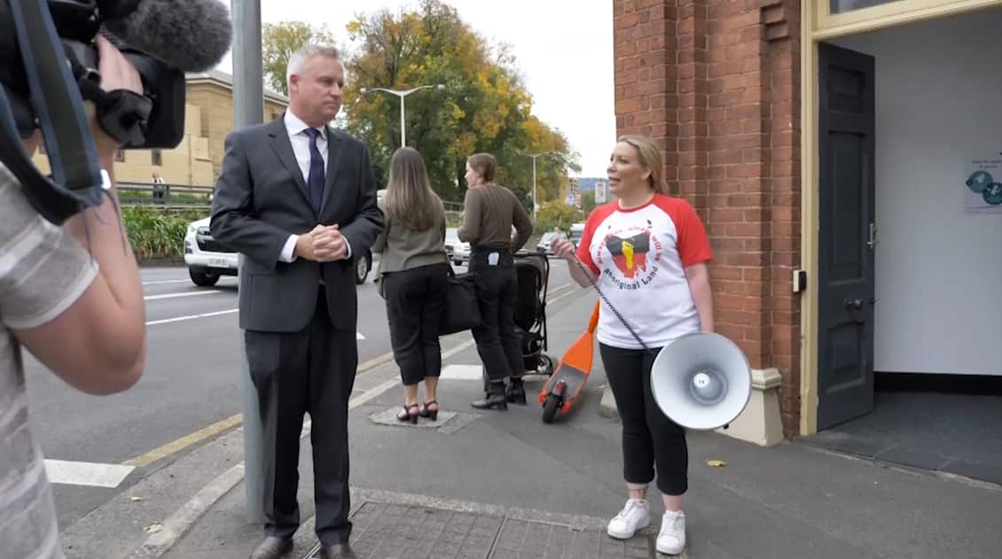 A woman holding a loudspeaker (right) standing outside a building next to a man in a suit.