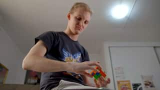 a man in a black t-shirt working on a Rubik's cube in his bedroom