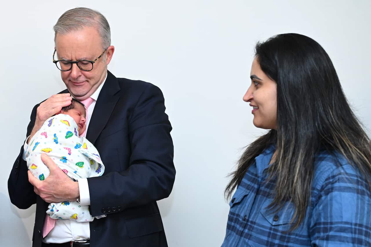 Anthony Albanese holds a small swaddled baby as a woman looks on.