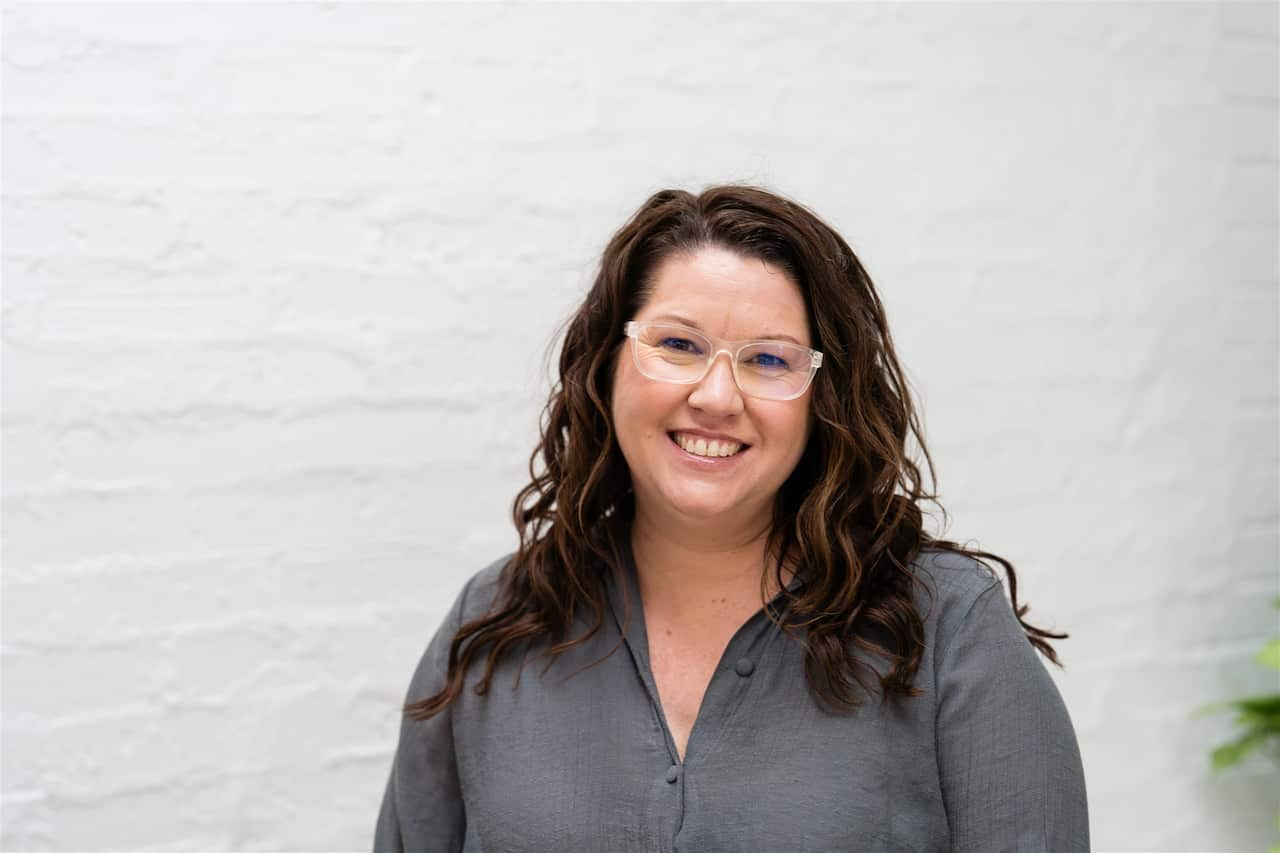 A woman with long hair, wearing glasses and smiling.