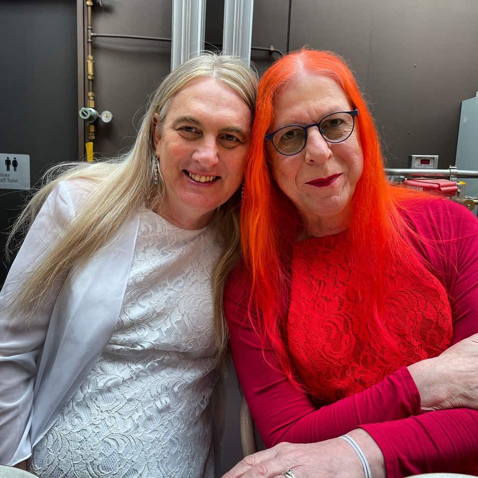A woman wearing a white dress and a woman wearing a red dress sitting close together.