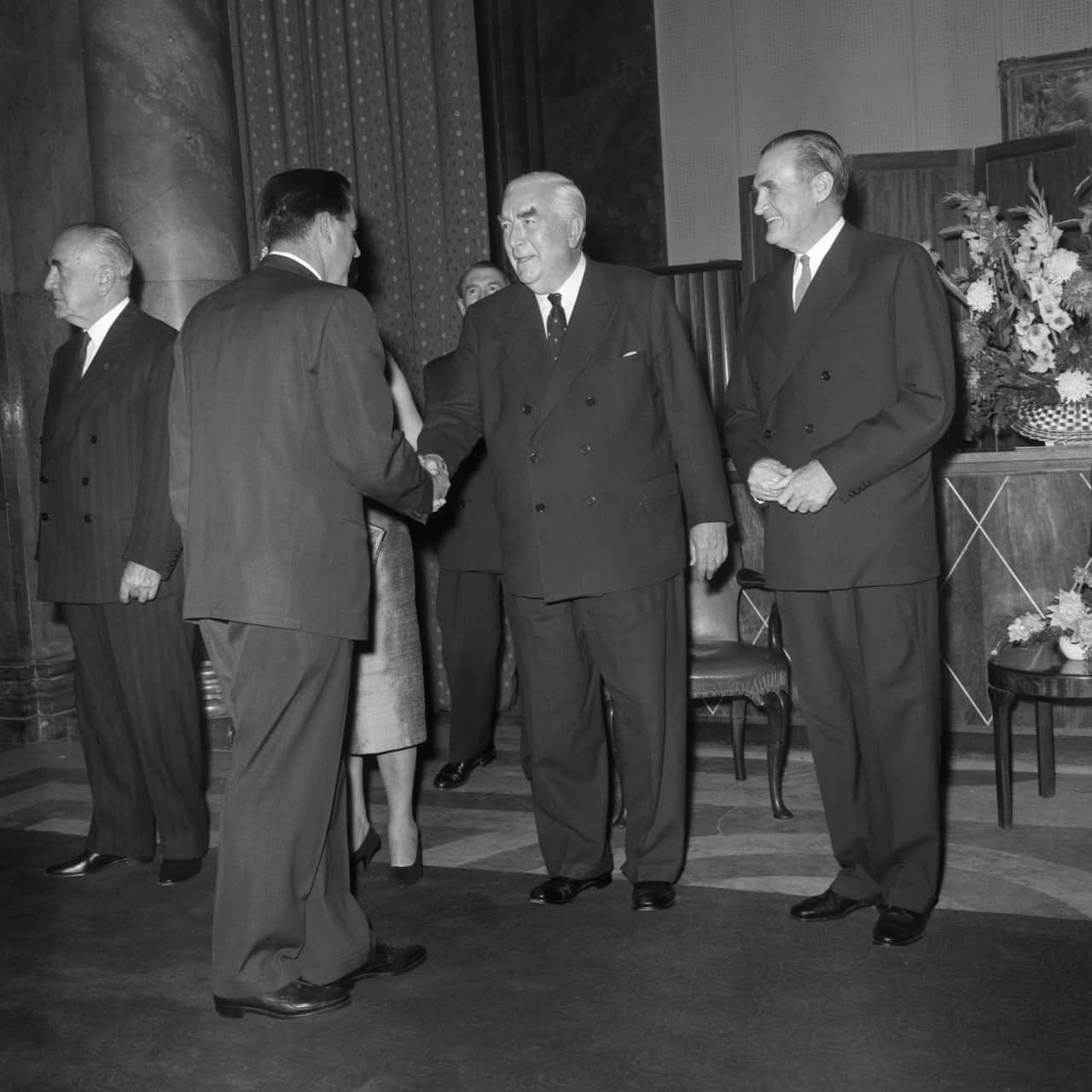 Men in suits in a large room. Two of them are shaking hands.