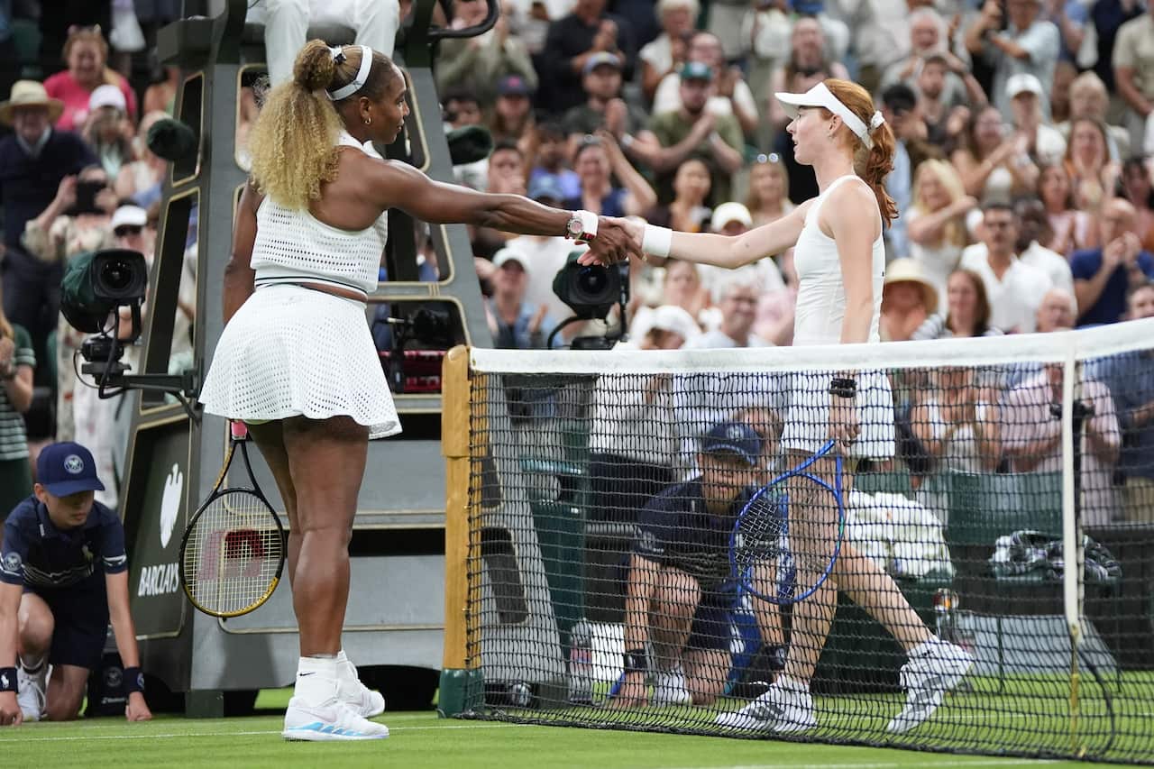 Two female tennis players dressed in white shake hands over the net