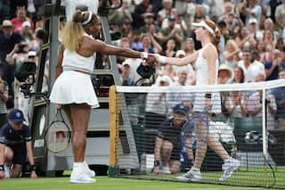 Two female tennis players dressed in white shake hands over the net