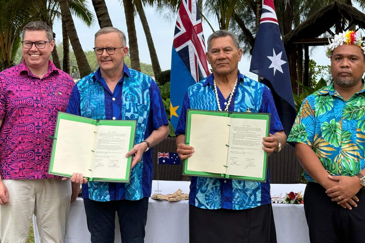 Four men wearing colourful shirts are pictured, holding documents. 