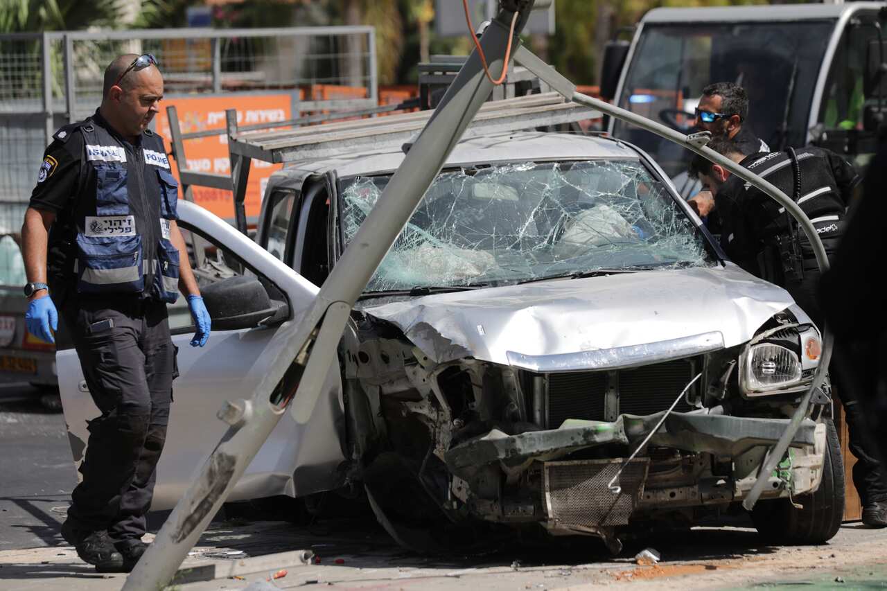 Israeli security and emergency personnel inspect a heavily damaged car