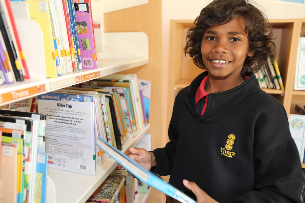A young boy holding a book next to a shelf of books in a library.
