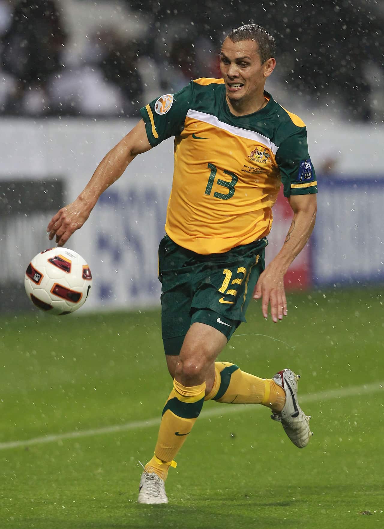 jade north on the pitch in socceroos grenn and gold uniform with his eyes on the ball.