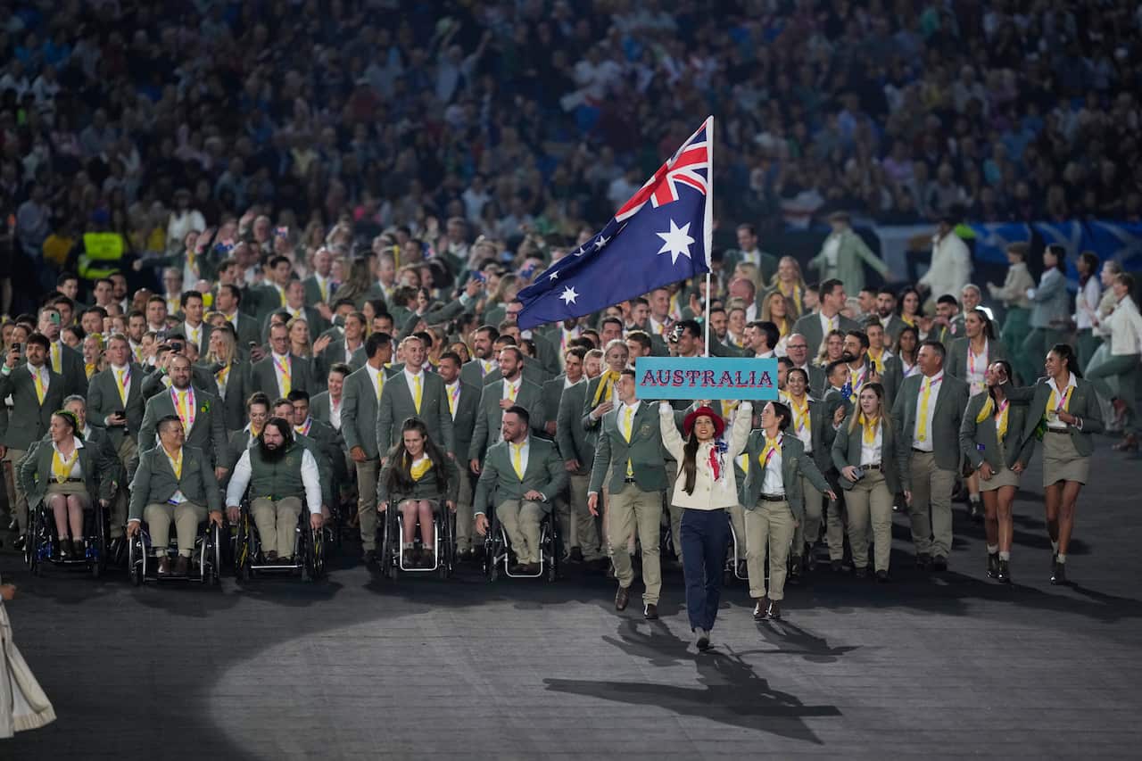 A crowd of people wearing green and khaki suits enter a stadium. The Australian flag is raised high. 