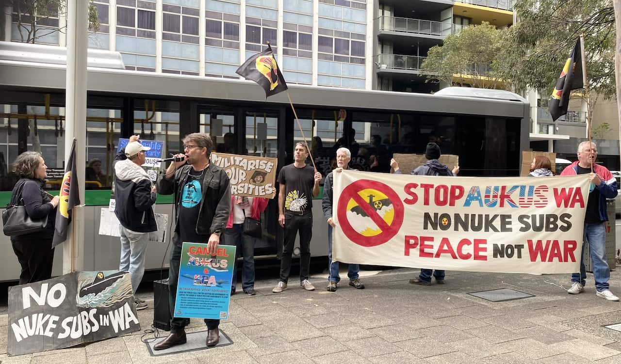 A group of protesters holding signs, outside a Perth hotel where a conference is being held.