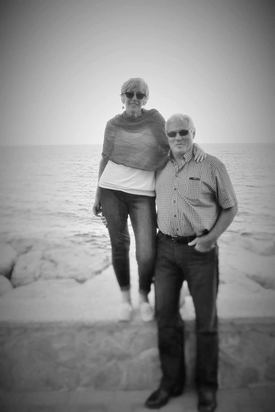 A happy couple standing by a wall next to the sea.