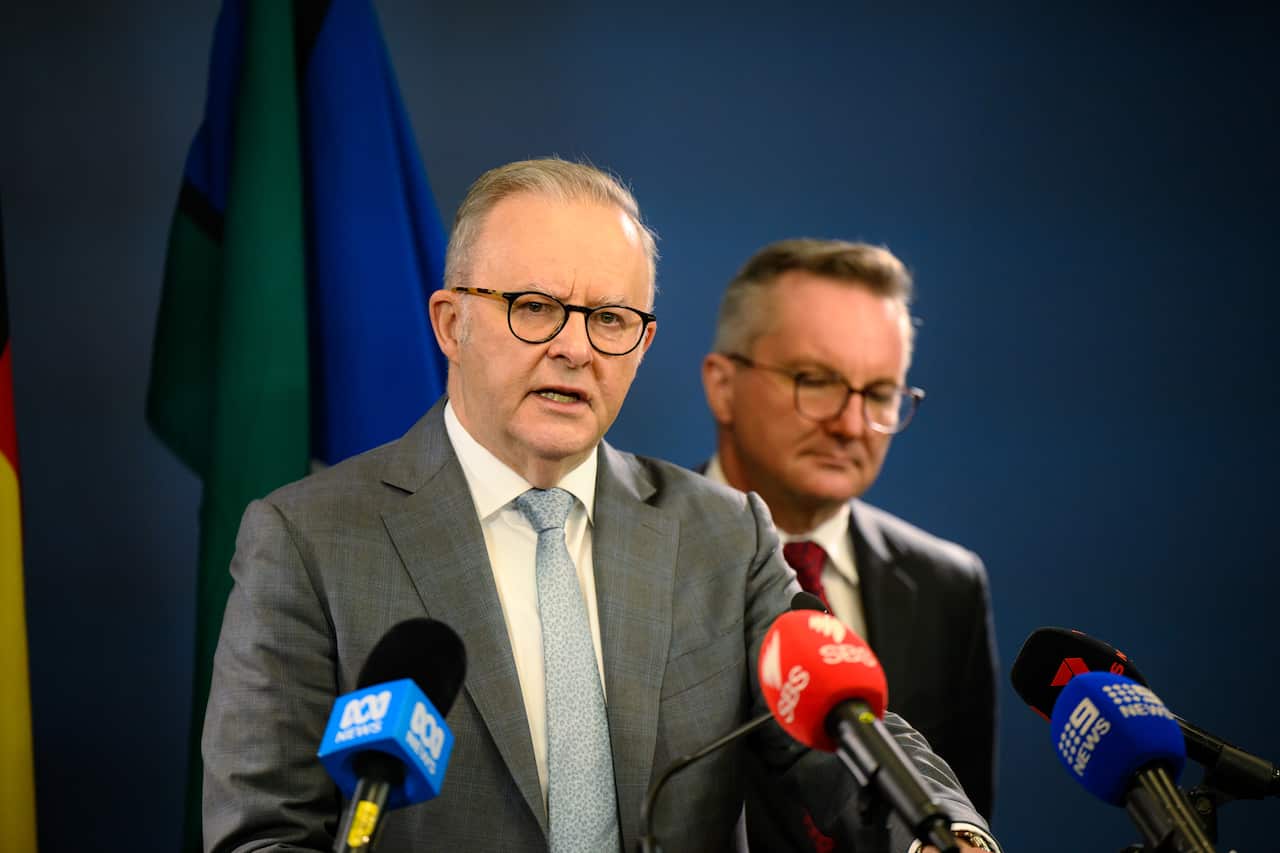 Two men wearing suits stand behind microphones