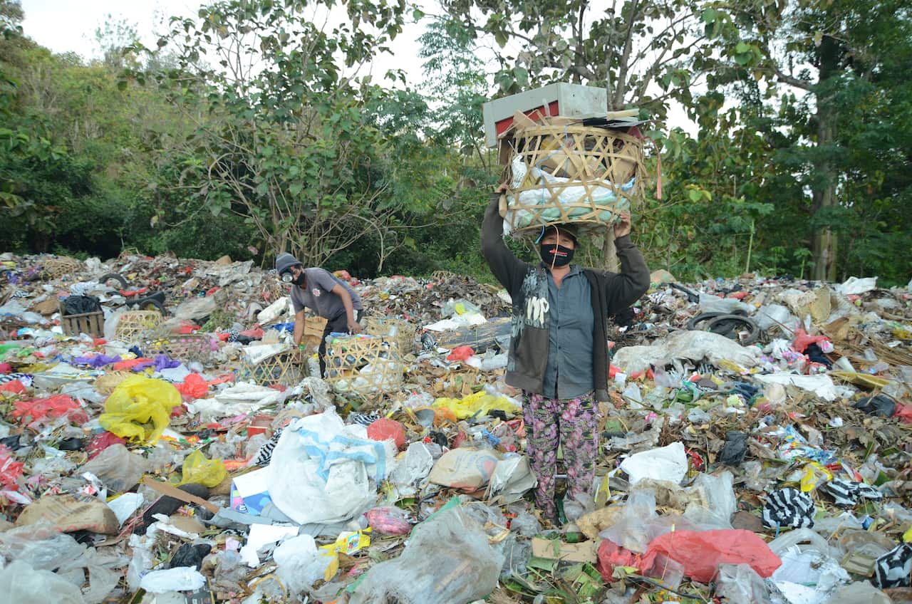 A man in a field of rubbish holding a basket of rubbish above his head