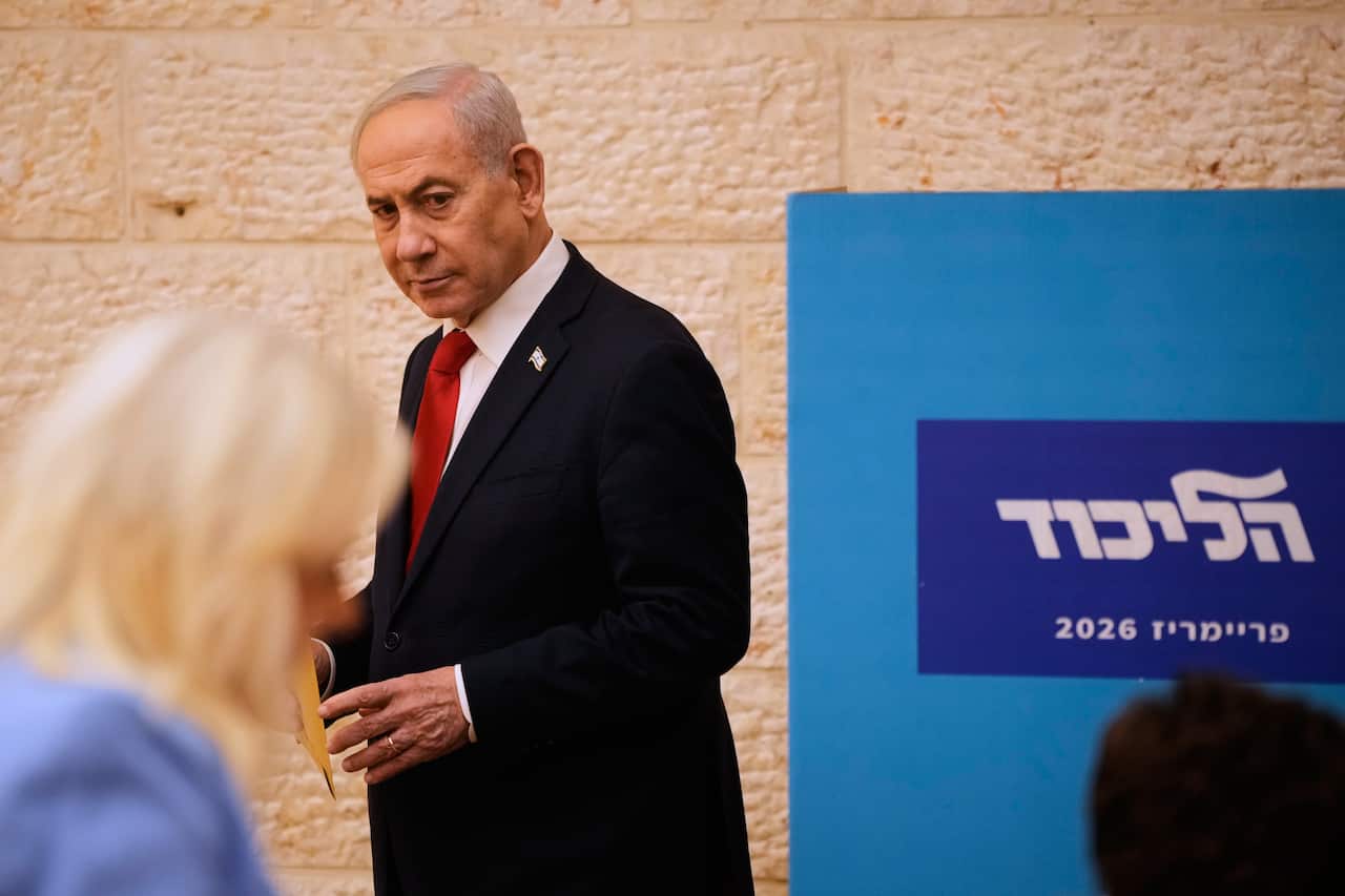 Benjamin Netanyahu, wearing a black suit and a red tie, looks sideways.