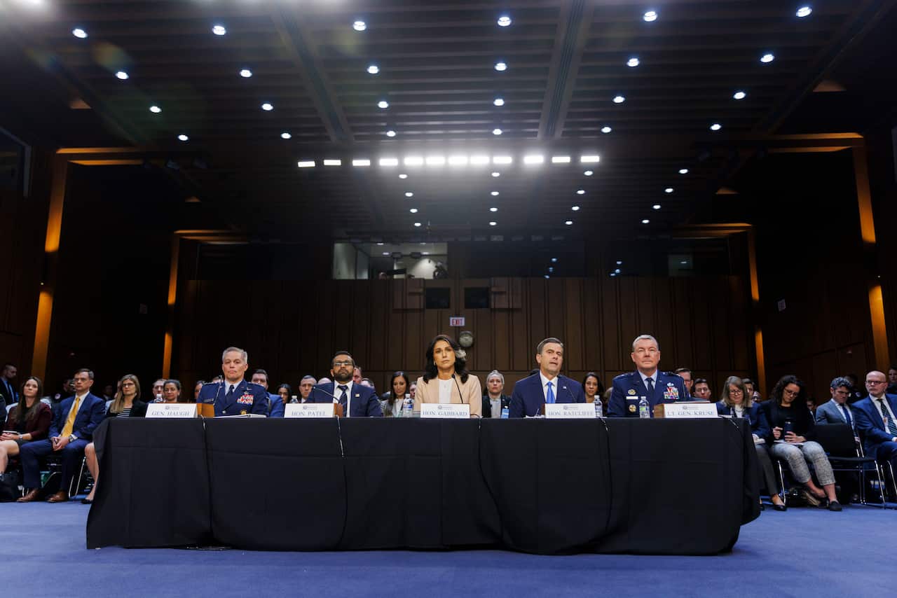 Five people sit at a table with name cards and microphones in large room full of people.
