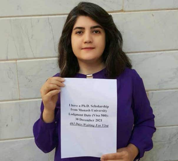 A woman holds a piece of paper saying she has a scholarship but is waiting for a visa